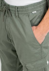 Pantalones cargo verdes de algodón con cinturilla elástica, cierre de cuerda, bolsillos laterales y detalle de bolsillo cargo en el muslo.