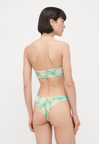Bikini szett, amely strapabíró felsőből és alacsonyan fazonozott alsóból áll, könnyű anyagból készült, zöld és sárga virágmintával.