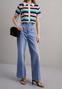 Randig stickad kort jumper med korta ärmar, tillsammans med högmidjade vida ljusblå jeans och svart vadderad handväska.