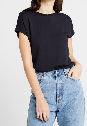 Marineblaues Kurzarmoberteil mit einem gezackten Ausschnitt, kombiniert mit hellblauen, hoch taillierten Jeans mit Knopfverschluss und Vordertaschen.