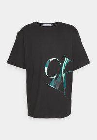 Black cotton t-shirt featuring a large, glossy turquoise "CK" graphic on the front. Crew neckline and short sleeves.