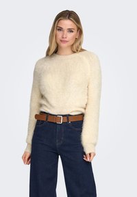 Cream-colored fluffy sweater with a round neckline and long sleeves, paired with dark blue high-waisted jeans and a brown leather belt.