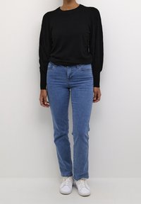 Svart stickad tröja med texturerade ärmar, kombinerad med ljusblå denimjeans och vita sneakers, med en klassisk, figursydd design.