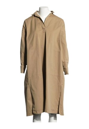 Robe chemise longue beige avec manches longues, col, ouvertures fendues à l’avant et coupe ample, présentée sur un mannequin blanc.