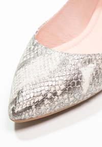 Chaussure plate à bout pointu avec un motif peau de serpent argenté et gris et une doublure intérieure rose clair.