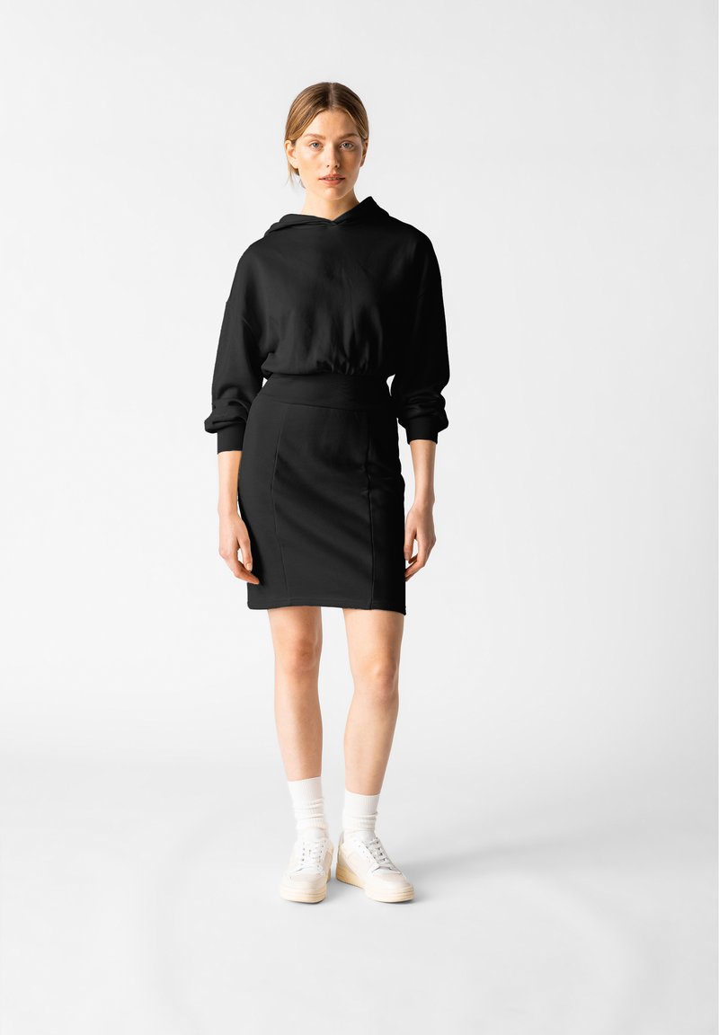 Svart hoodie med avslappnad passform och långa ärmar, parat med en svart pennkjol. Utrustad med vita sneakers och vita ankelsockor för kontrast.