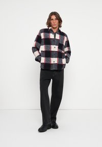 Karierte Flanellhemden in Marineblau, Weiß und Rot mit Knopfdesign. Das Modell trägt schwarze Jeans und schwarze Schuhe.