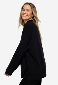 Navy oversized Pullover aus strukturiertem Strick mit langen Ärmeln, geripptem Saum und seitlichen Schlitzen. Kombiniert mit schwarzen, unifarbenen Hosen.