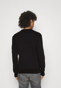 Felpa nera con maniche lunghe, polsini e orlo a coste, design semplice, indossata con jeans grigi, vista da dietro.