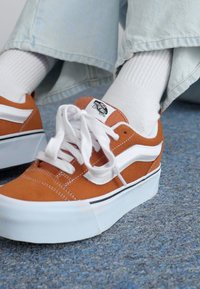 Orange ruskind sneakers med hvide detaljer, med flad sål, rund tå og snørebånd. Tekstureret overdækning og logo synligt på tungen.