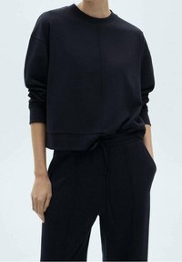 Sweat-shirt noir court avec col rond et manches oversize, fabriqué en tissu texturé. Associé à un pantalon de jogging assorti à taille élastique avec cordon de serrage.