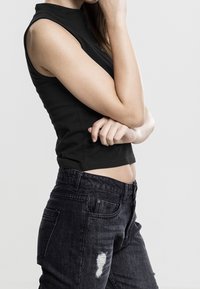 Top noir sans manches associé à un jean en denim foncé avec un design déchiré. L'ensemble présente une silhouette cintrée.