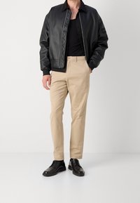 Giacca bomber nera in faux pelle con polsini a coste, chinos color sabbia e scarpe lace-up in pelle nera. Design minimalista con un'apparenza elegante.