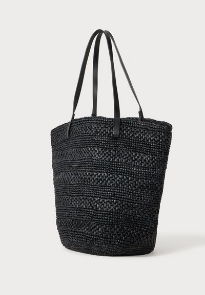Sac cabas tissé noir avec longues poignées en cuir, ouverture supérieure spacieuse et motif à rayures horizontales texturées.