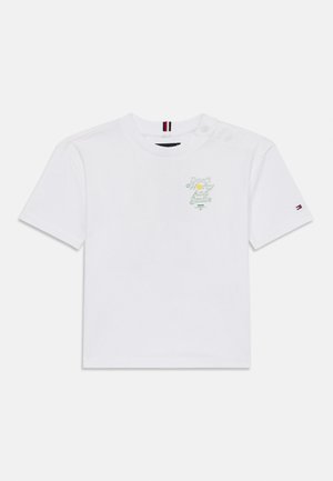 Bela bombažna majica s kratkimi rokavi, na kateri je napisan "Ne skrbite in se smejte" z zelenim besedilom ter črtastim poudarkom v bližini vratu na eni strani.