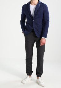 Námořnický pletený blazer s jedním knoflíkem, klopou a dvěma předními kapsami, doplněný tmavými tapered kalhotami a bílými teniskami.
