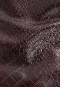 Burgundy leather featuring a textured crocodile pattern, with a glossy finish highlighting the surface details and depth.