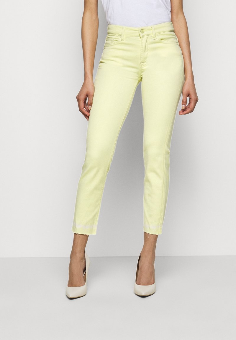 Jeans de mezclilla amarillo claro con un corte slim y longitud recortada, con un dobladillo deshilachado y diseño de cuatro bolsillos, combinados con tacones altos beige.