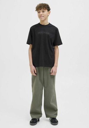 Zwarte katoenen T-shirt met "ORIGINALS" in het grijs gedrukt, gecombineerd met losse olijfgroene broeken. Model draagt zwarte sneakers, tegen een neutrale achtergrond.