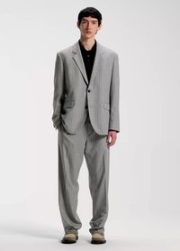 Lysegråt jakkesæt med tynde striber, bestående af en tætsiddende blazer og løse bukser. Bæres over en sort poloshirt, suppleret med beige sko.