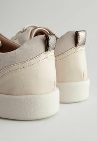 Beige Leder-Sneaker mit strukturiertem Rücken, grauem Akzent an der Ferse und einer weißen Gummisohle. Verfügt über gestickte Details und eine weiche Oberfläche.