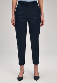 Pantaloni blu navy scuri con fit su misura, dotati di una parte anteriore piatta, tasche laterali e orlo con risvolto, realizzati in un tessuto liscio.