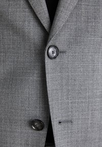 Blazer grigio con tessuto testurizzato, dotato di due bottoni neri e rever a punta. Dettagliato con un motivo sottile e vestibilità sartoriale.