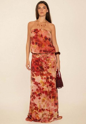 Mujer con vestido sin tirantes, fluido, de flores rojas y naranjas, sosteniendo un bolso rojo tejido, con collar y pulsera como accesorios.
