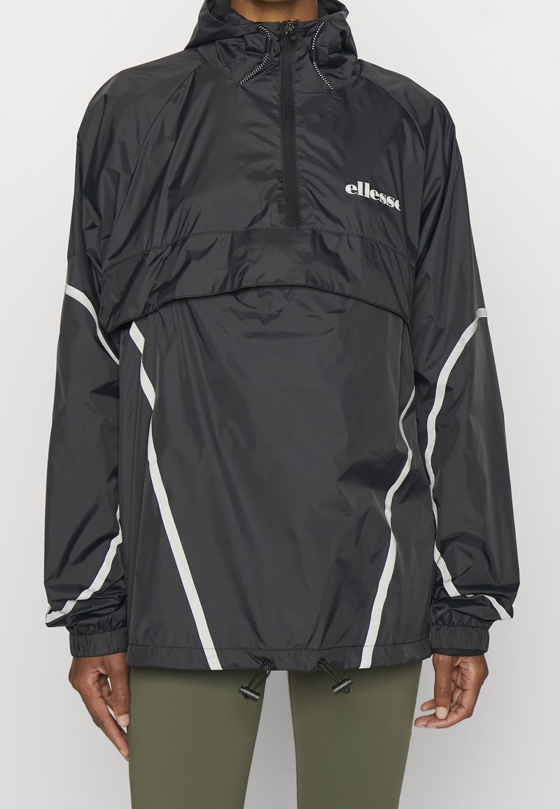 Veste coupe-vent noire avec capuche, présentant des rayures diagonales blanches, une fermeture éclair frontale et un ourlet ajustable. Conçue pour une coupe ample.