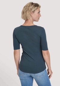Teal fitted t-shirt met korte mouwen, ronde hals, lichtgewicht stof en een gladde textuur. Achteraan is een licht gebogen zoom zichtbaar.