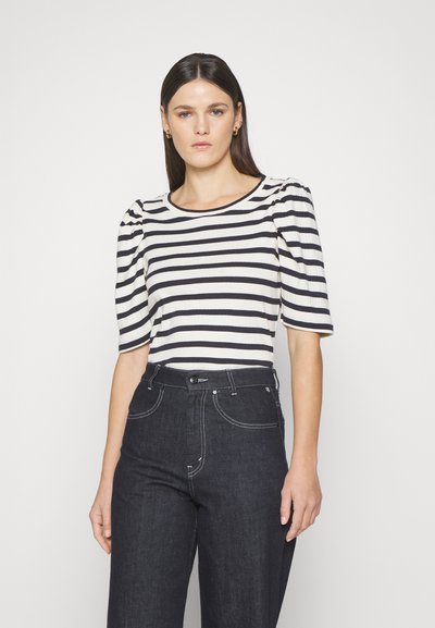 Striped, ribbed top in cream and navy with puff sleeves. Paired with dark denim jeans featuring a high waist and contrast stitching.