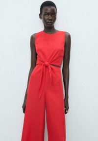 Red sleeveless jumpsuit with a knot detail at the waist, featuring wide-legged pants and a smooth fabric finish.