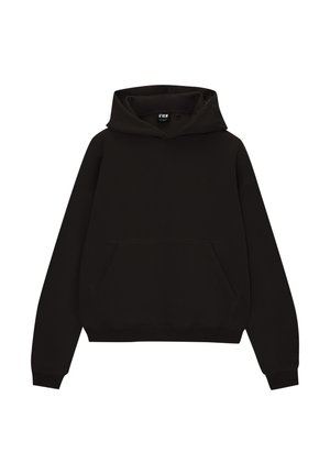 Person trägt einen schwarzen Kapuzenpullover mit Fronttasche und hellblaue Jeans mit weitem Bein, steht mit einer Hand in der Tasche.