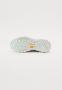 Terrengsko såle med teksturert, mønstret gummi i mintgrønn med rosa detaljer. Vibram-logoen synlig i gult.