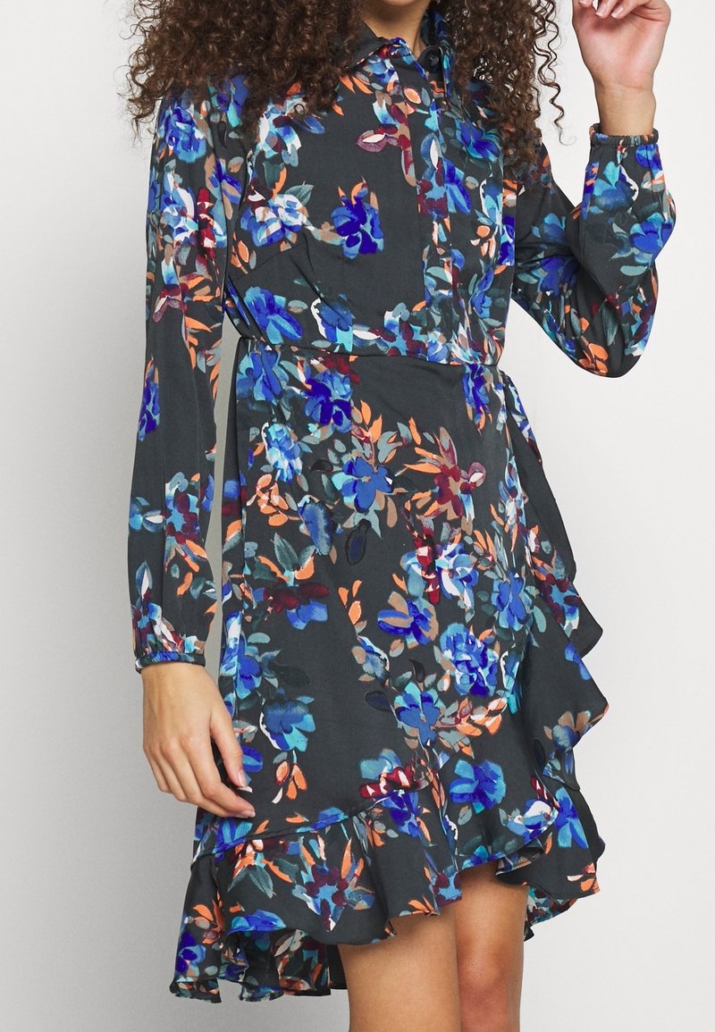 Robe fleurie en gris foncé avec des motifs bleus, orange et verts. Dotée d'un col, de manches longues et d'un ourlet à volants. Tissu léger.