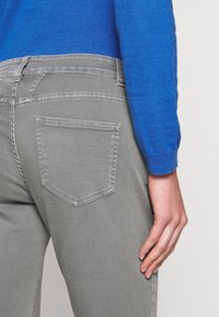 Szare dżinsy o gładkiej fakturze, z jedną tylną kieszenią i kontrastującym przeszyciem, połączone z niebieskim swetrem dzianinowym.