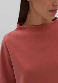 Dusty rose-colored top with a rounded neckline, made from a smooth fabric, featuring a relaxed fit and soft texture.