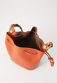 Borsa a secchiello in pelle arancione con finitura testurizzata, hardware dorato e tracolla regolabile. L'apertura superiore rivela un morbido interno marrone.