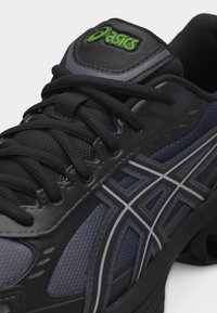 Close-up of black and dark blue ASICS running shoe featuring black laces and green ASICS logo on the tongue.