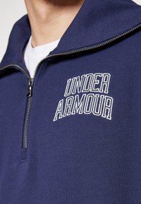 Sudadera deportiva de media cremallera en azul marino con tejido texturizado, que presenta el logo blanco "UNDER ARMOUR" en el pecho y una cremallera metálica.