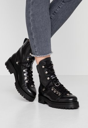 Bottes chevauchées en cuir noir avec des œillets métalliques, fermeture à lacets et semelles robustes. Présente une texture lisse et des accents en métal argenté.