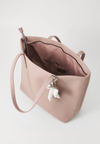 Sac fourre-tout rose en matériau lisse avec fermeture éclair, poche intérieure et charm décoratif. Poignées doubles. Forme rectangulaire simple.