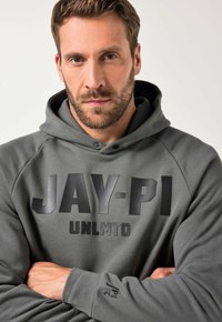 Šedá mikina s kapucí a černým textem "JAY-PI UNLMTD," s texturovanou tkaninou, pulovrovým designem a šňůrkami na kapuci.