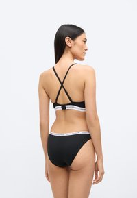 Fekete fehérnemű szett, amely vékony keresztezett pántos melltartóból és márkázott elasztikus szalagból áll, hozzáillő, magas derekú alsóval.