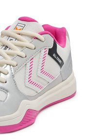 Zapatilla deportiva gris con un diseño de malla, acentos en rosa y detalles a rayas. Incluye un cuello acolchado y una suela texturizada para mayor agarre.