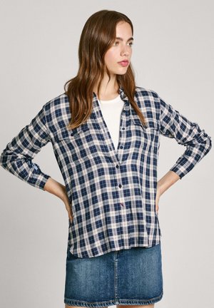 Navy- und weiße karierte Hemdbluse mit langen Ärmeln, ausgestattet mit einem Kragen und Taschenakzenten, getragen über einem weißen T-Shirt und einem Jeansrock.