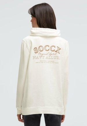 Cream hooded sweatshirt featuring a large brown graphic text "SOCCX Original Spirit NAVY ALLURE" on the back, with cuffed sleeves and relaxed fit.