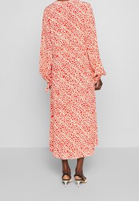 Červené a bílé šaty s potiskem, dlouhými rukávy, volným střihem a splývavým siluetu, doplněné černobílými špičatými podpatky.