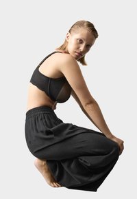 Sort blonde-bh med meshpaneler kombineret med løse sorte bukser med en elastisk, rynket talje. Glat tekstur over det hele.