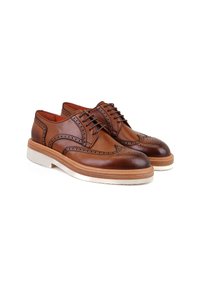 Chaussures brogue en cuir marron avec des perforations détaillées, bout rond et semelle blanche contrastante. Présente un design classique à lacets.